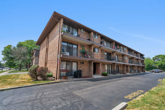 Front view of a three-story brick apartment building with balconies.