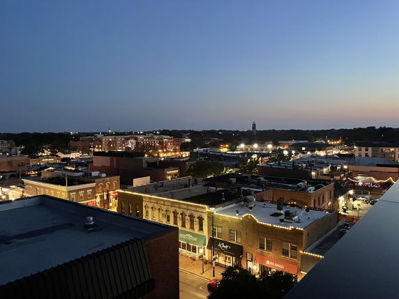 Panoramic view of a town at dusk with buildings and lights visible.