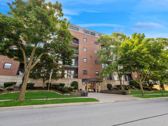 Front view of a multi-story brick building with balconies and trees in front.