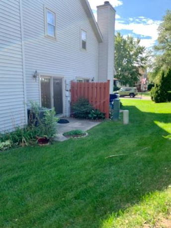 Side view of a two-story house with a small patio and grass lawn.