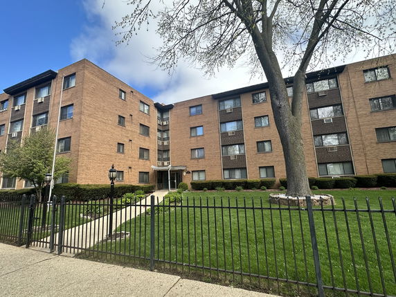 Front view of a multi-story brick apartment building with multiple windows and a central entrance.