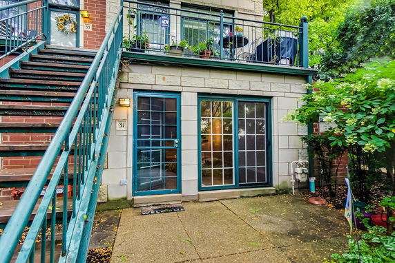 Front view of a townhouse with a staircase leading to the upper level and a patio area on the ground floor.