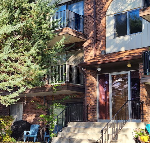 Front view of a multi-story brick building with balconies and a staircase leading to the entrance.