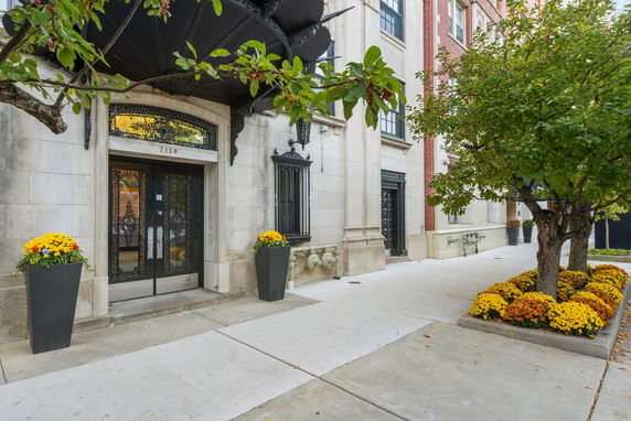 Front view of a building entrance with decorative metal doors and potted plants.