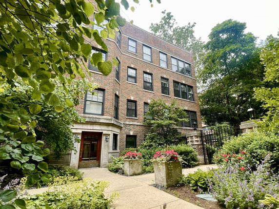 Front view of a multi-story brick building with lush greenery and plants around.