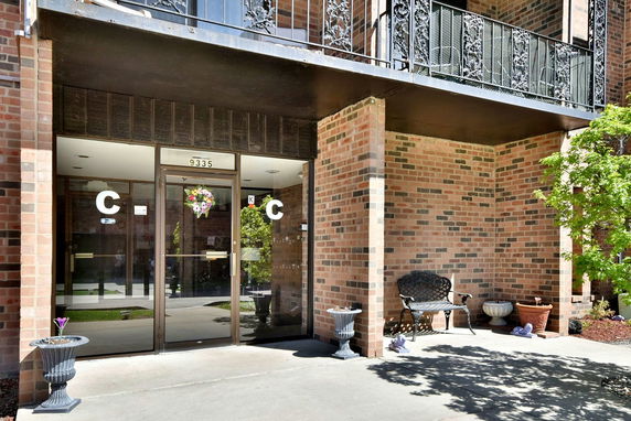 Front view of a brick building entrance with glass doors and a balcony above.
