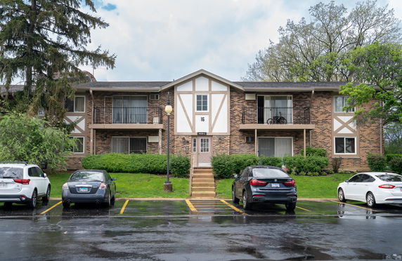 Front view of a two-story brick apartment building with balconies and stairs leading to the entrance.