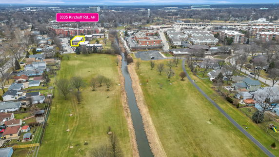 Aerial panoramic view of a residential area with houses, apartment buildings, and open green spaces, along with a canal running through the landscape.