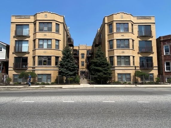 Front view of a multi-story apartment building with a central entrance and bay windows.