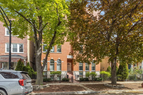 Front view of a multi-story brick building with arched windows and trees lining the street.