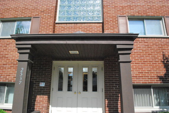 Front view of a brick building with a covered entrance and white double doors.