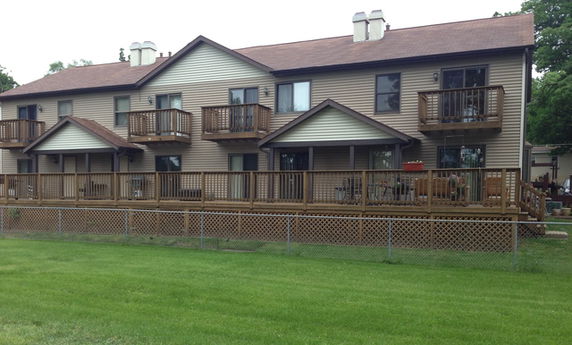 Front view of a two-story residential building with multiple balconies and a wooden deck.