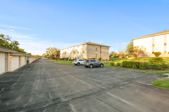 Outdoor parking area with parked cars next to garages and apartment buildings.