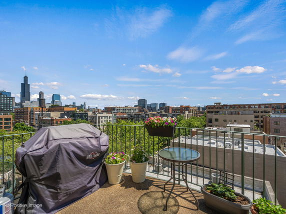View of a cityscape from a rooftop patio with a grill and potted plants.
