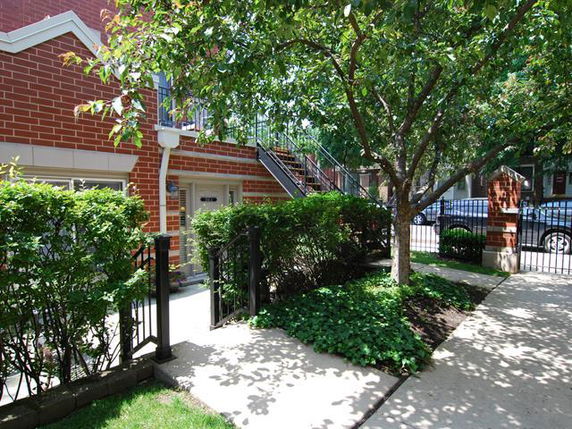 Front view of a brick building with stairs and greenery.