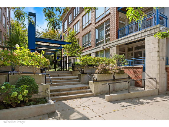 Front view of a multi-story brick building with steps leading to the entrance and planters with greenery.