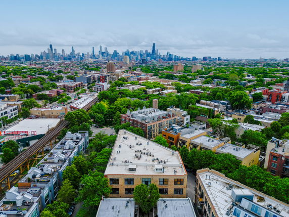 Aerial view of a cityscape with high-rise buildings in the distance and green areas interspersed with urban structures.