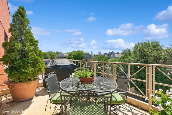 Outdoor terrace with a table and potted plants, overlooking a cityscape.