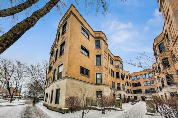 Front view of a multi-story brick apartment building with multiple windows and an entrance courtyard.
