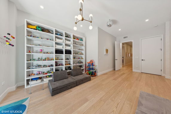 A room with wooden flooring featuring a large shelving unit filled with toys and small sofas, indicative of an indoor play area.