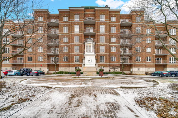 Front view of a multi-story brick apartment building with balconies and a central clock tower.