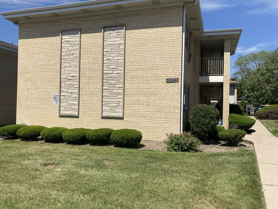 Front view of a two-story brick building with textured stone panels and a walkway.