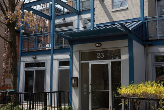 Front view of a modern multi-story building with large windows and a blue framework.