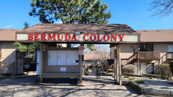 Front view of a residential building with a covered signpost labeled 'Bermuda Colony' and mailboxes.