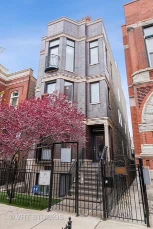 Front view of a multi-story building with a small balcony and black metal fence.