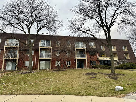 Front view of a three-story apartment building with balconies and a brick facade.