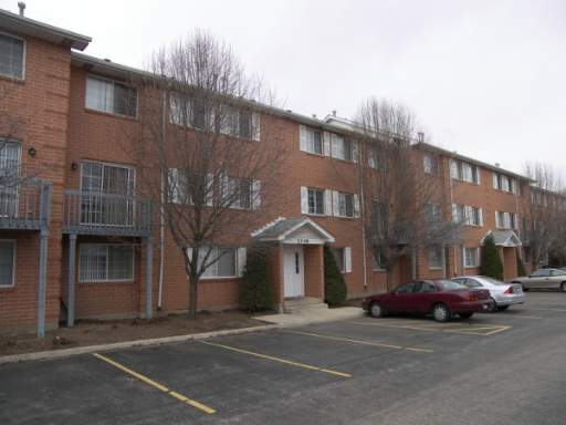 Front view of a three-story brick apartment building with multiple balconies and a parking area.