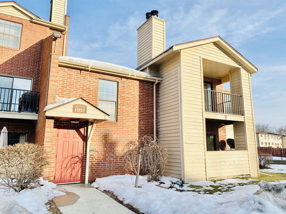Front view of a multi-story brick building with a red door and balconies.