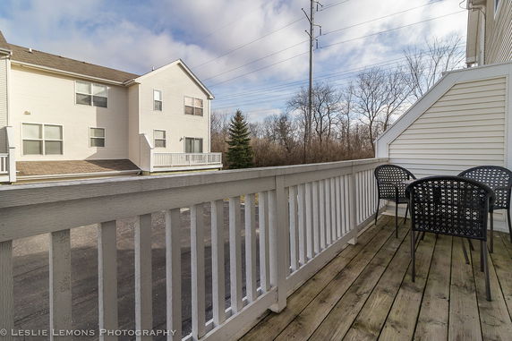 View of a multi-story house with a deck and outdoor furniture, surrounded by trees.