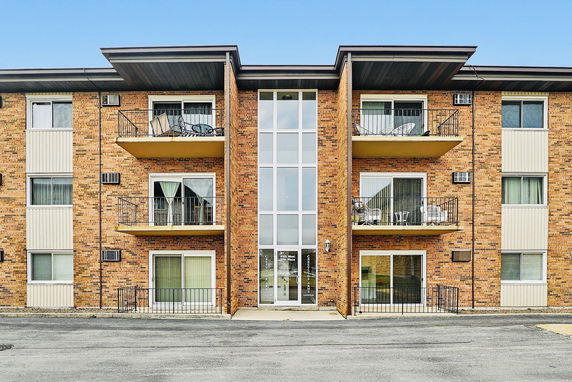 Front view of a multi-story apartment building with balconies and brick facade.