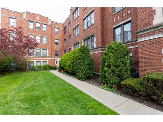 Front view of a multi-story brick apartment building with a landscaped garden.