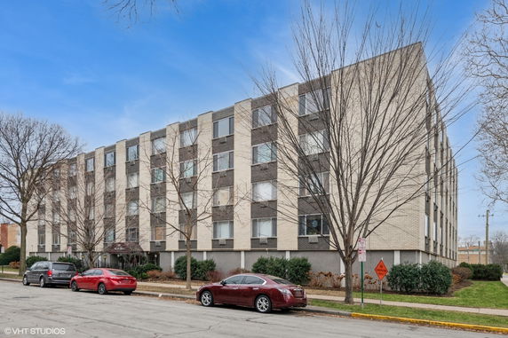 Front view of a multi-story apartment building with numerous windows and parking area in front.