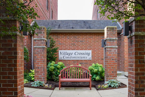 Front view of a building with a brick exterior and a sign reading 'Village Crossing Condominiums.'