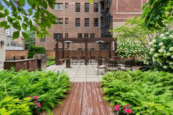 Rooftop garden area with seating and a barbecue grill, surrounded by plants and trees.