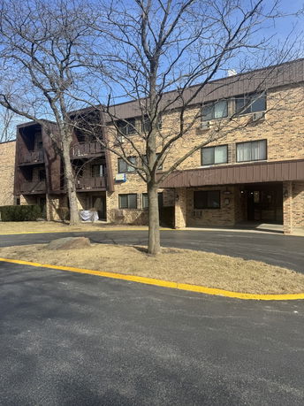 Front view of a brick apartment building with balconies and trees.