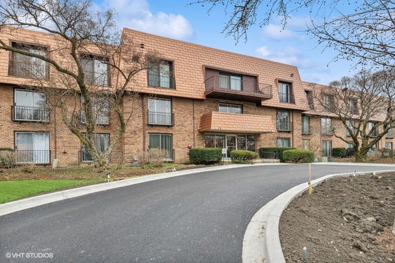 Front view of a multi-story brick building with balconies and a driveway.
