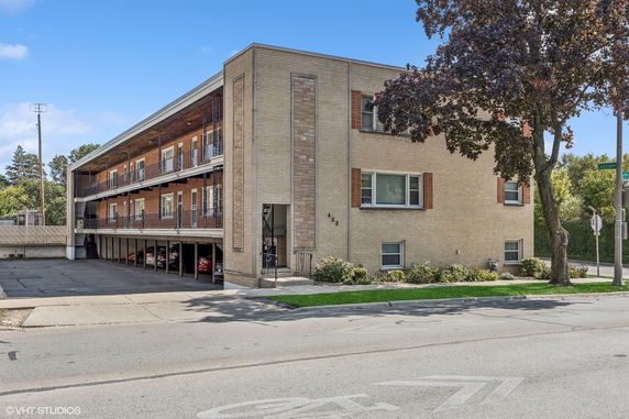 Front and side view of a two-story apartment building with brick exterior and covered parking below.