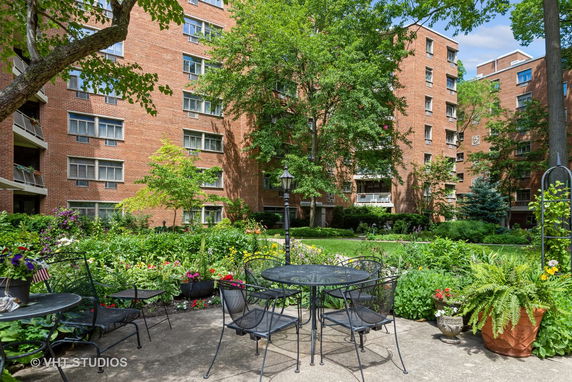 Outdoor view of brick apartment buildings with gardens and patio seating.