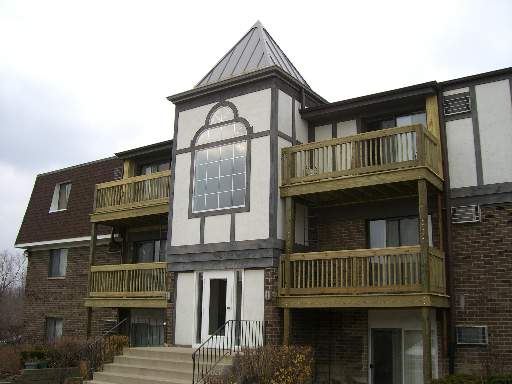 Front view of a multi-story building with wooden balconies and a distinctive triangular roof section.