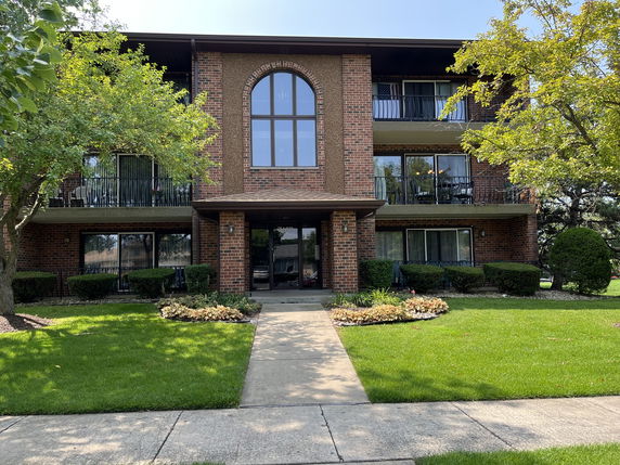 Front view of a three-story brick apartment building with balconies.
