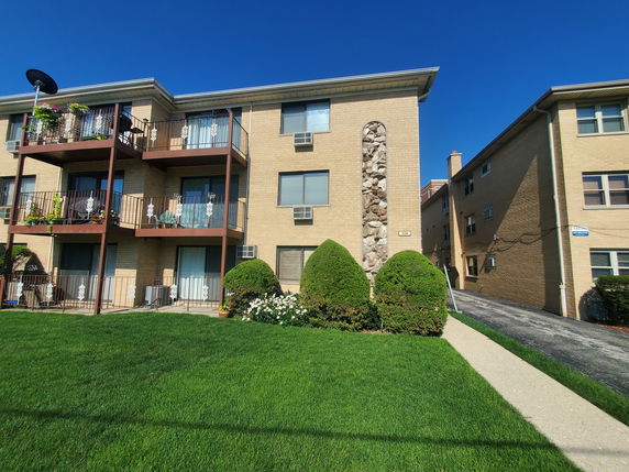 Front view of a multi-story apartment building with balconies and brick exterior.