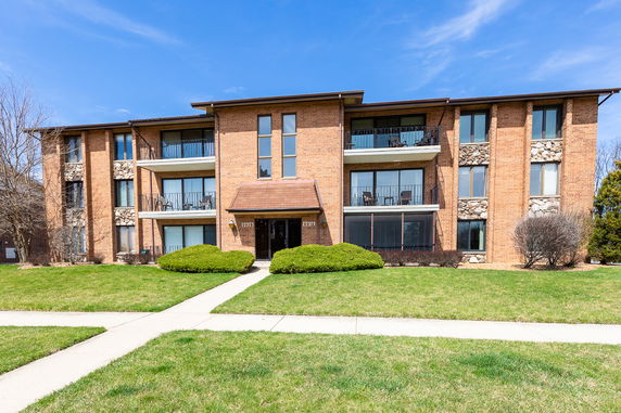 Front view of a three-story brick apartment building with balconies.