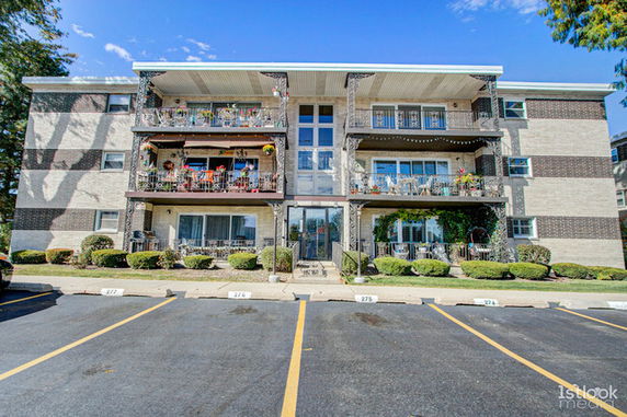 Front view of a three-story apartment building with balconies and a parking area.