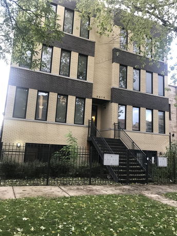 Front view of a multi-story brick building with large windows and staircase entrance.