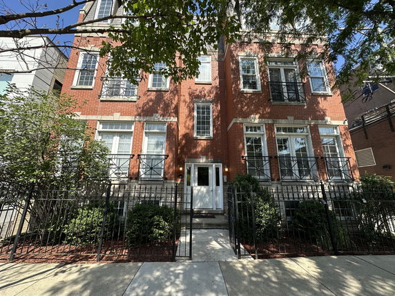 Front view of a multi-story brick building with balconies and a gated entrance.