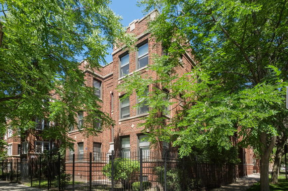 Front view of a residential brick building with multiple windows and trees surrounding it.